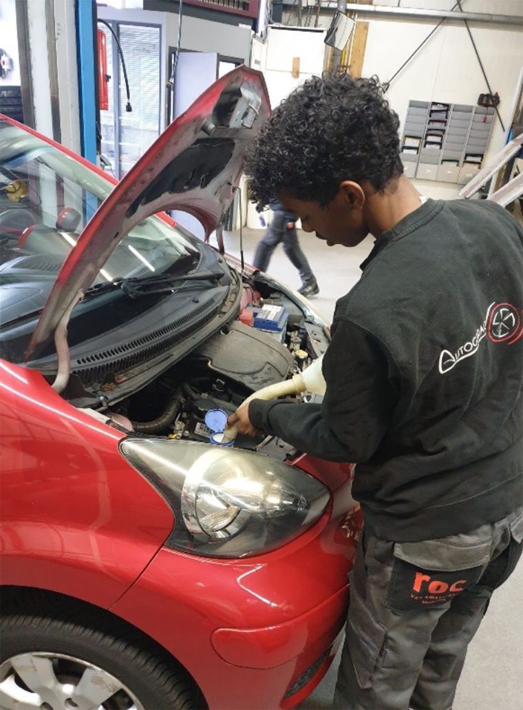 Leerling die aan een auto motor werkt