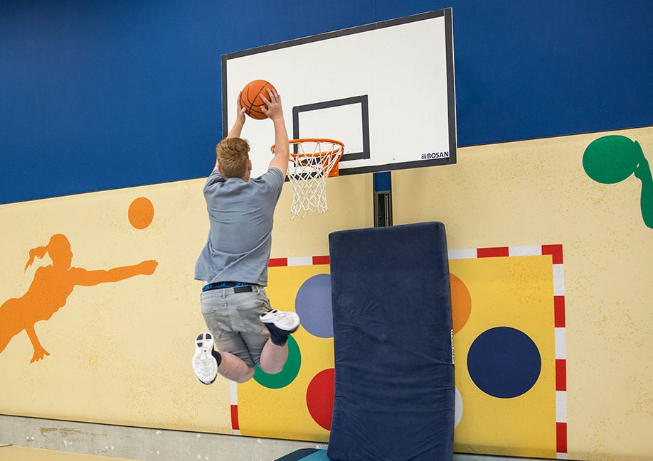 Een jongen die een bal in een basketbal korf gooit